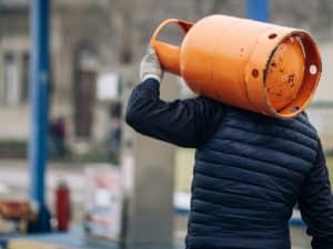 Person carrying an orange LPG cylinder on their shoulder, showcasing the portability of different lpg cylinder sizes.