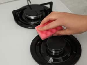 Hand cleaning a gas stove burner with a pink sponge, indicating maintenance for a gas stove not heating.