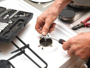 Technician using tools to fix gas stove igniter, adjusting burner parts for proper functioning.