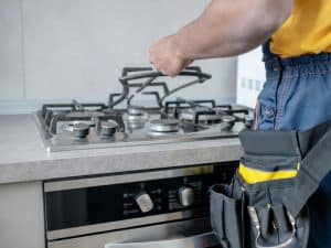 Technician lifting gas stove grate to fix gas stove igniter during a repair service.