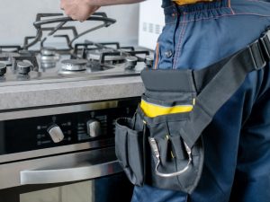 Technician inspecting a gas stove with tools, highlighting the importance of cleaning gas stove burners regularly.