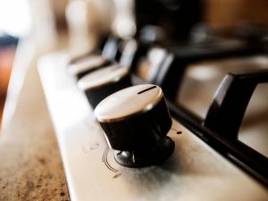 A close-up of a broken gas stove knob on a stainless steel cooktop.