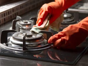 Person wearing gloves cleaning a gas stove burner to fix a gas stove weak flame and improve performance.