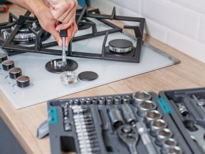 Technician repairing a gas stove burner, addressing a gas stove weak flame issue with tools on a kitchen counter.