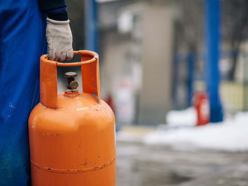 gloved hand holding orange gas bottle for installing lpg at home
