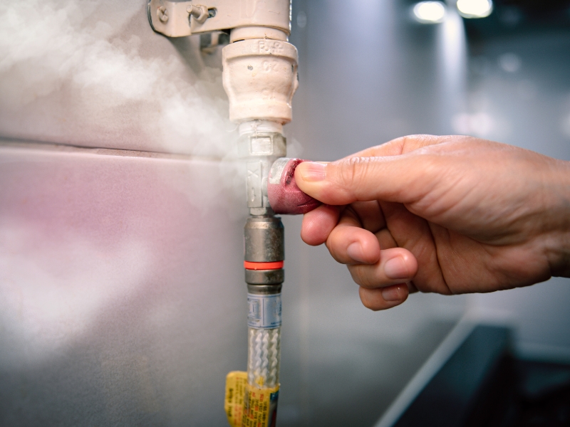 Hand turning off valve to stop suspected gas leak with visible white vapour emission.